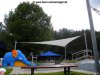 Ein großes beiges Sonnensegel in Dreicksform freistehend ausgeführt mit drei Segelmasten gibt Schatten über einem Kleinkindbecken im Freibad | Lisori Sonnensegel