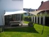 Ein weißes Sonnensegel von Lisori schützt eine Terrasse mit Holztisch und Stühlen. Im Hintergrund ist ein weißes Haus zu sehen. Die Befestigungen sind aus V2 Edelstahl. Ein stilvoller Ort zum Entspannen!