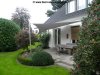 Dreieckiges graues Sonnensegel befestigt an 1 Aufhängepunkt an der Hausfassade sowie 2 Segelmasten von Lisori über der Terrasse eines Einfamilienhauses | Lisori Sonnensegel