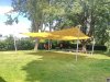 Ein großes gelbes Sonnensegel in Viereckform freistehend ausgeführt mit vier Segelmasten beschattet eine Rasenfläche auf einer Außenfläche im öffentlichen Raum | Lisori Sonnensegel