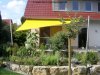 Viereckiges gelbes Sonnensegel befestigt an 2 Aufhängepunkten am Haus sowie 2 Segelmasten von Lisori über der Gartenterasse eines Einfamilienhauses | Lisori Sonnensegel