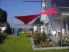 Viereckiges rotes Sonnensegel befestigt an 1 Aufhängepunkt an der Hausfassade sowie 3 Segelmasten von Lisori über hochgesetzer Terasse mit Treppe eines Einfamilienhauses | Lisori Sonnensegel