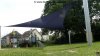 Ein großes blaues dreieckiges Sonnensegel freistehend ausgeführt mit drei Segelmasten beschattet einen Spielplatz auf der Grünfläche eines Freibads | Lisori Sonnensegel