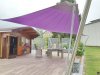 Grosses aufrollbares Sonnensegel in lila, freistehend ausgeführt mit 4 Edelstahl-Segelmasten über einer grossen Terrasse im Garten